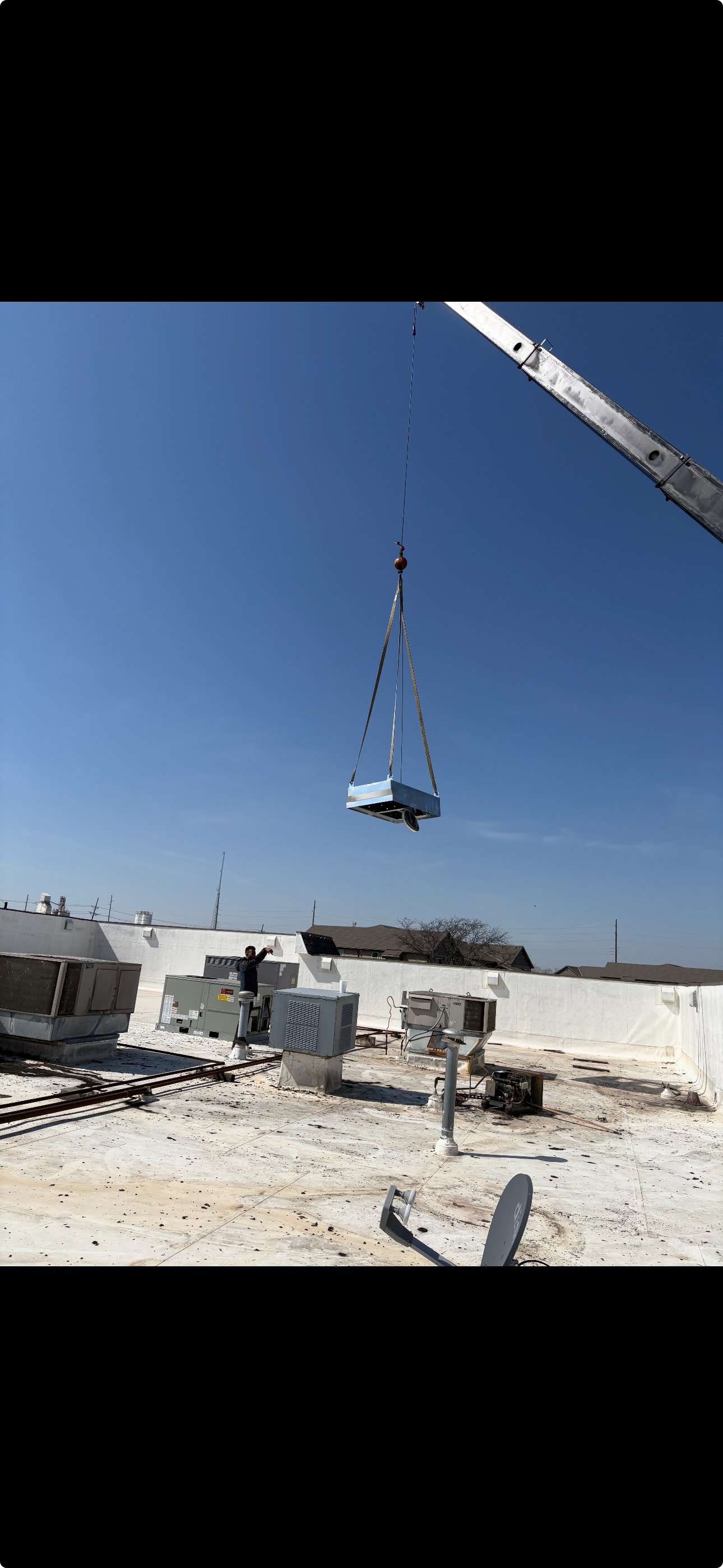 Crane lifting an HVAC unit onto a commercial rooftop.